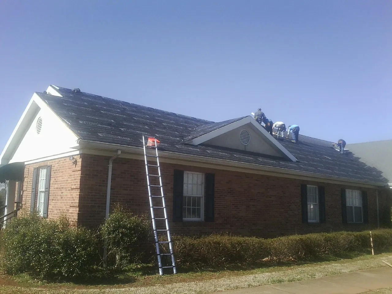 Crew tearing shingles off a brick ranch roof with a ladder set — Emergency Roof Repair work by our crew in New London